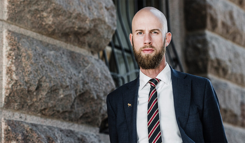 Carl-Oskar Bohlin, minister för civilt försvar står framför en stenbyggnad i mörk kavaj och slips